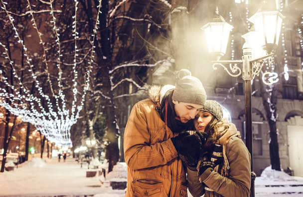 Young couple drinking hot tea in the city center under illumination - Photo, Image
