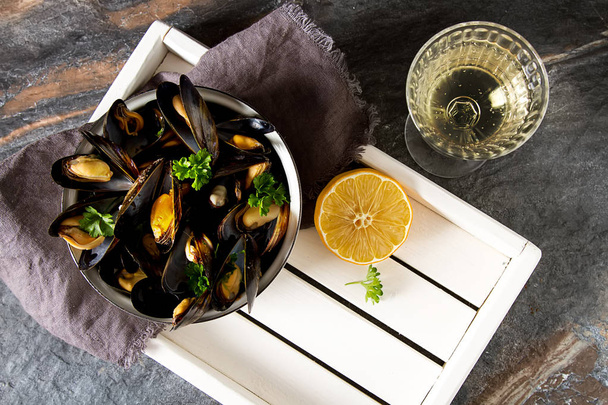 Mussels with herbs in a bowl with lemon and wine on a white wood - Фото, изображение