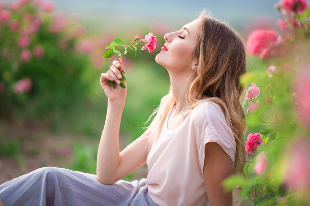 Mooi jong meisje is het dragen van casual kleding met rust in een tuin met roze bloesem rozen - Foto, afbeelding