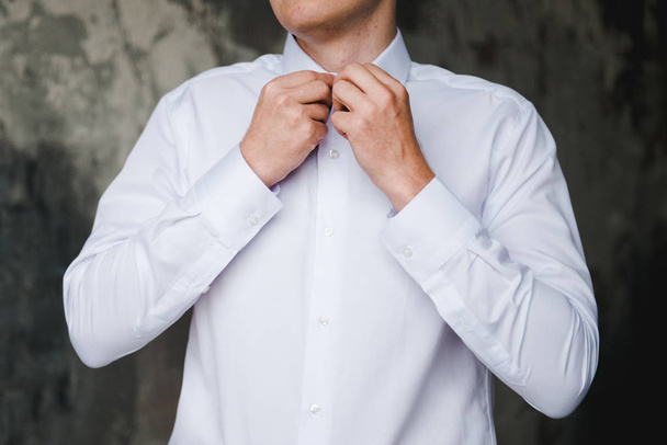 Morning of the groom. Groom morning preparation. Young and handsome groom getting dressed in a wedding shirt  - 写真・画像