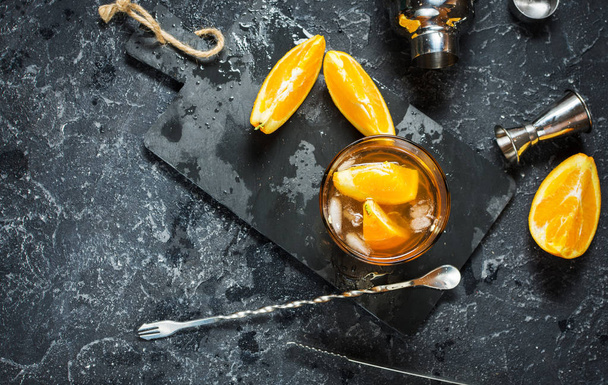 A glass of Negroni cocktail with orange and lemon. Alcoholic drink with rum and vermouth on dark stone table. - Фото, изображение