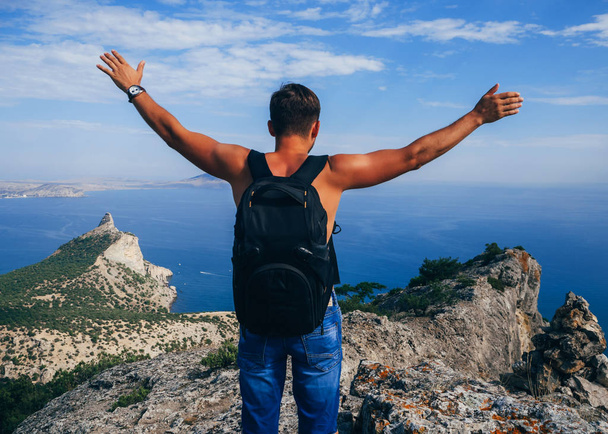 man traveler with backpack standing on top of a mountain with hands raised up - Photo, Image