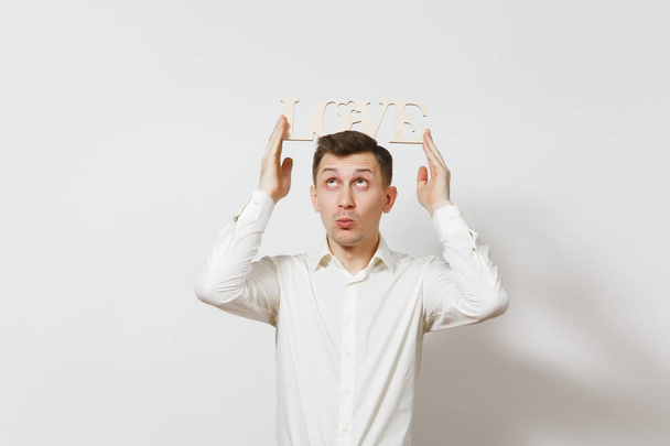 Young confused man in shirt holding above head wooden word Love isolated on white background. Copy space for advertisement. St. Valentine's Day, International Women's Day, birthday, holiday concept. - Photo, Image
