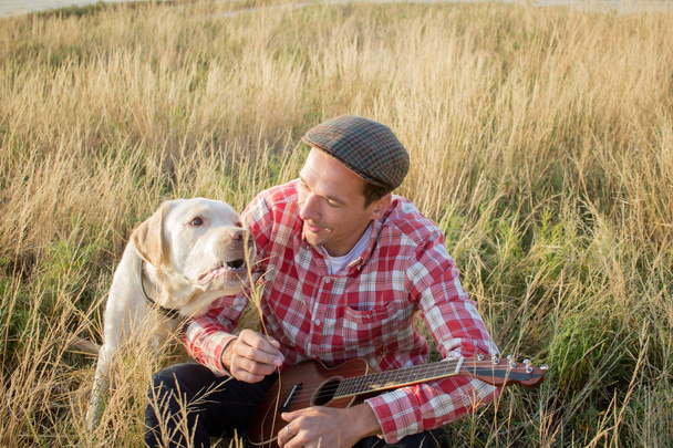 Young hipster and golden labrador dog having good time in the fields and play on ukulele - Foto, Imagem
