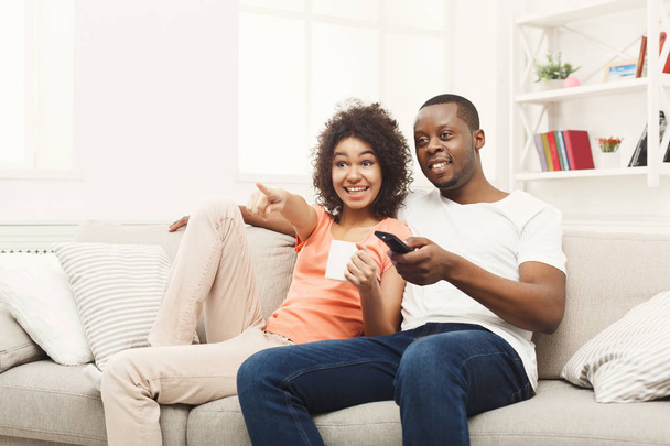 Улыбающаяся африканско-американская молодая пара смотрит телевизор дома
 - Фото, изображение