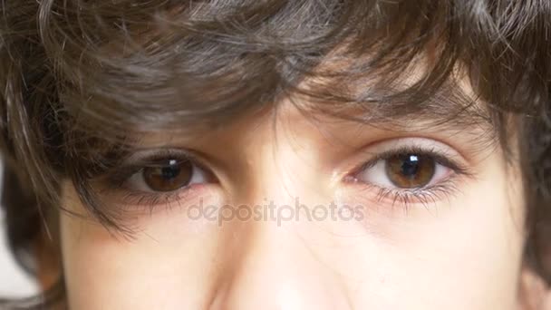 Brązowe oczy chłopca z długie, czarne rzęsy. on wygląda spod długie kręcone Kosmyk. 4 k, zwolnionym tempie, zbliżenie - Materiał filmowy, wideo