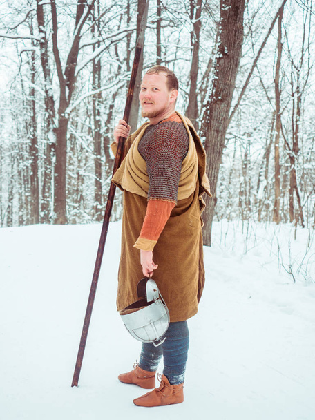 チェーン メールとヘルメットで中世アイルランドの戦士が冬の森で槍を保持します。 - 写真・画像