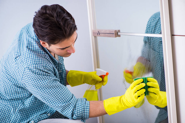 Joven hombre limpieza espejo en casa hotel - Foto, Imagen