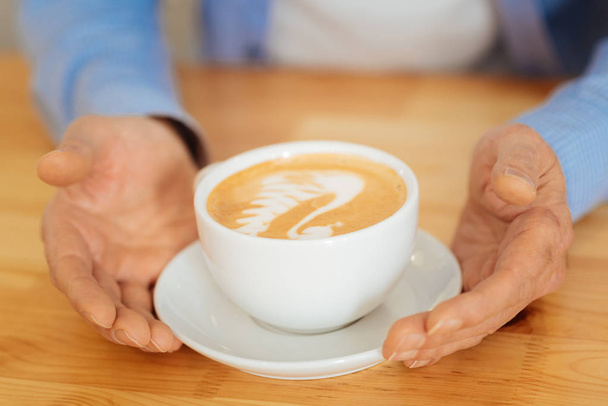 Senior calm man sitting and holding hands near a cup. - Фото, зображення