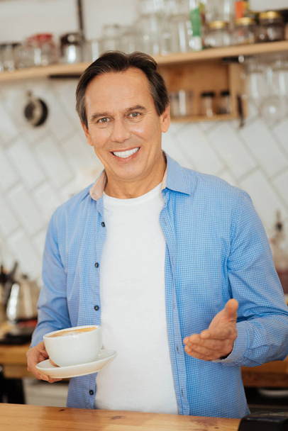 Smiling intelligent man holding a cup and gesticulating. - Foto, Bild