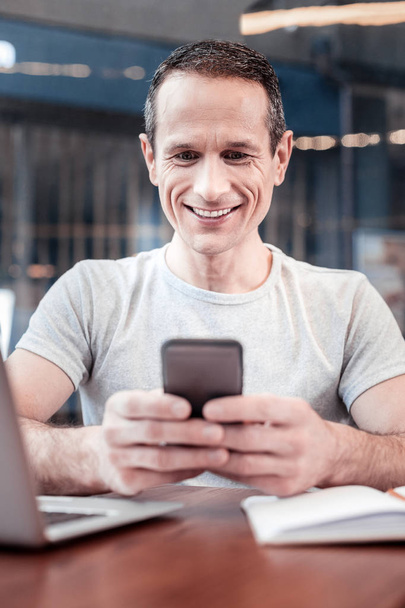Handsome brunette smiling while messaging - Фото, изображение