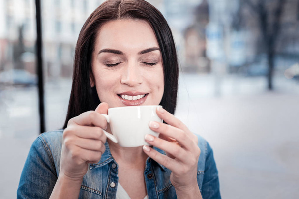 Portrait of delighted girl that smelling good coffee - 写真・画像