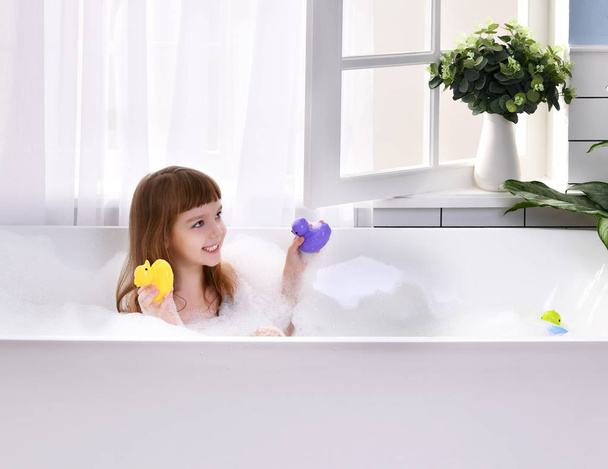  Happy little baby girl sitting in bath tub playing with duck toys  in the bathroom - Foto, Bild
