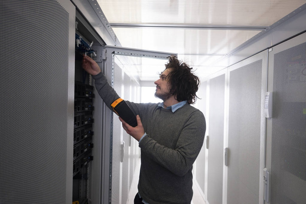 young IT technician using digital cable analyzer on server in large data center - Foto, afbeelding
