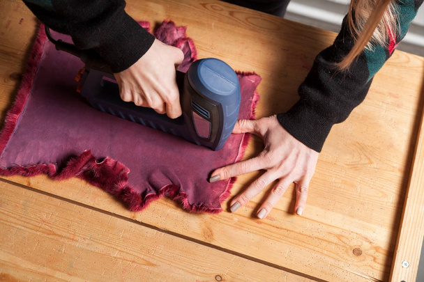 Un primer plano de una joven peluquera seca una máquina especial con piel natural para hacer el abrigo de piel de una mujer. El proceso de hacer el abrigo de piel de una mujer
 - Foto, Imagen
