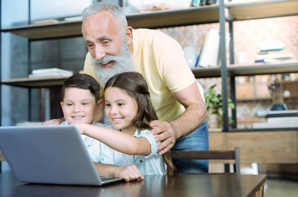 Cheerful grandfather using laptop with his grandchildren - Fotó, kép
