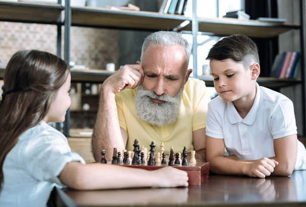 Nachdenklicher Rentner spielt Schach mit Enkeln - Foto, Bild