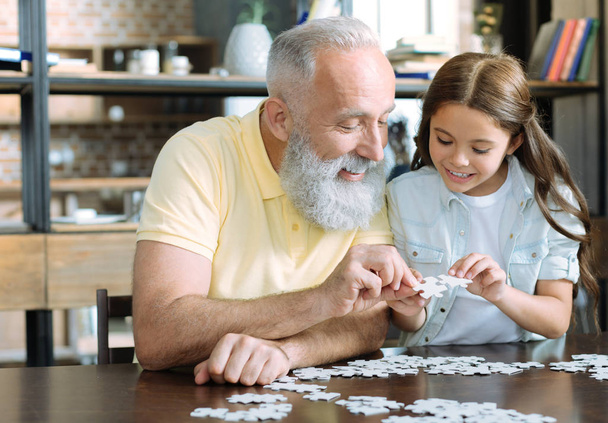 Grandfather and girl chatting while playing jigsaw puzzle - Fotoğraf, Görsel