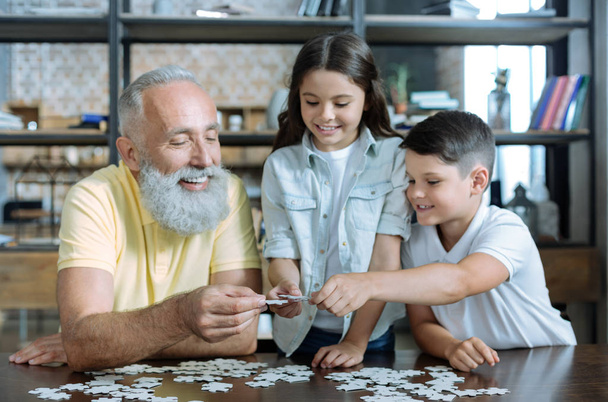 Thoughtful elderly man and grandchildren putting puzzle together - Foto, Bild