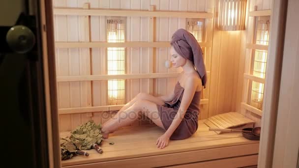 Genç kadın bir saunada dinlendirici bir havlu ile giyinmiş. Yeni Fin saunası, tıbbi prosedürler, Klasik Ahşap sauna için kızılötesi paneller iç. - Video, Çekim
