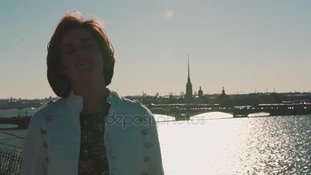 Menina bonita em jaqueta branca no telhado com vista panorâmica do rio da cidade
 - Filmagem, Vídeo
