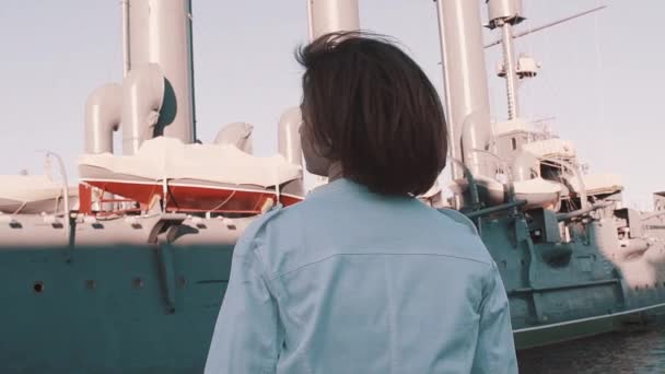 Joyful young woman in summer dress turns around in front of old battleship - Footage, Video