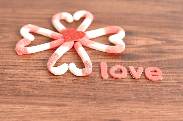 Un patrón de flores hecho de bastones de caramelo lleno de formas de corazón con un pequeño corazón rojo en el centro y la palabra amor
 - Foto, Imagen