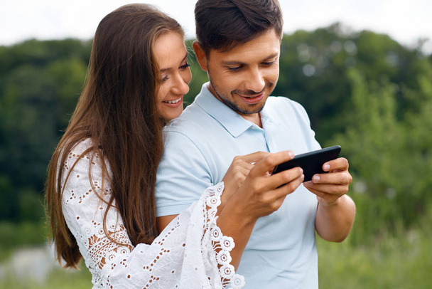 Couple In Love. Man And Woman Looking At Phone In Nature. - Photo, Image