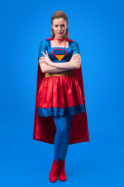 attractive woman in superhero costume with arms crossed isolated on blue - Photo, Image