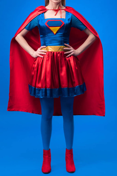 partial view of woman in superhero costume standing akimbo isolated on blue - Foto, immagini