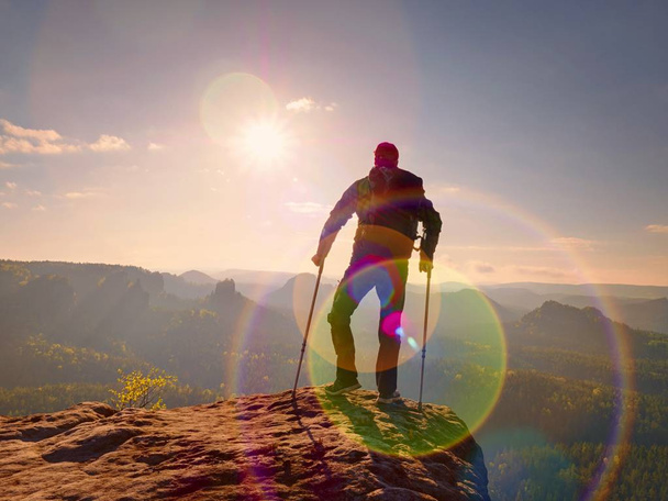 Be winner. Man tourist after accident use knee brace features  and forearm crutches. Man looking over valley to Sun hang at horizon. - Photo, Image