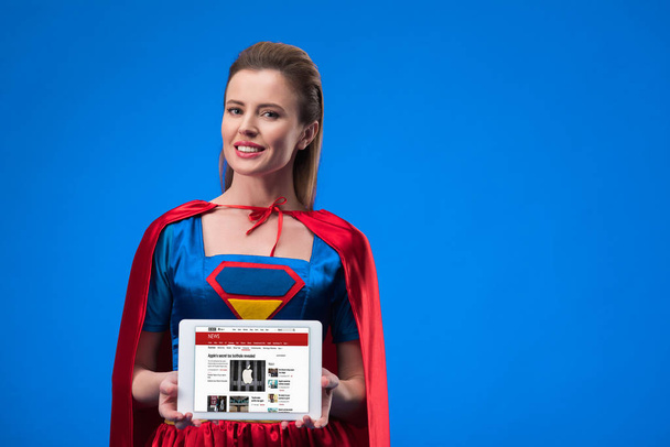 Porträt einer fröhlichen Frau im Superheldenkostüm mit Tablet isoliert auf blauem Grund - Foto, Bild