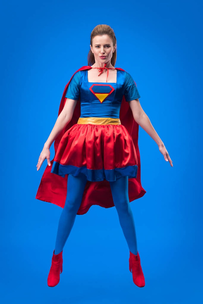 beautiful superwoman in costume jumping isolated on blue - Foto, imagen