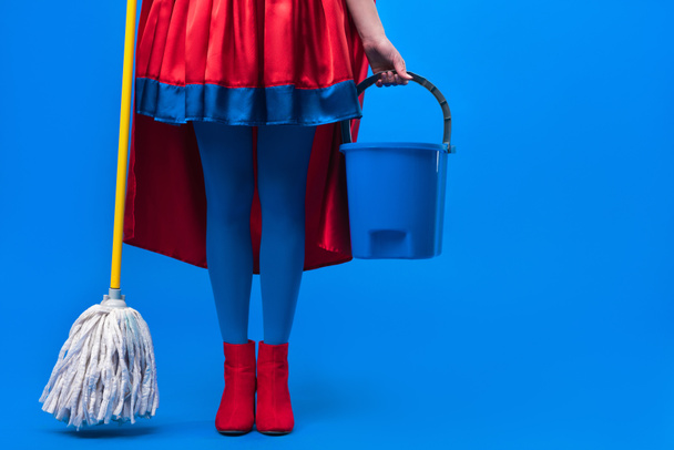 partial view of woman in superhero costume with mop and bucket for cleaning isolated on blue - Foto, Bild