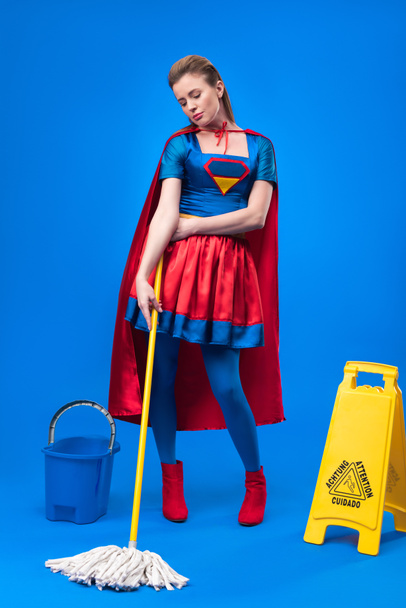 aantrekkelijke vrouw in superheld kostuum met Let op teken, emmer en dweil voor het reinigen van geïsoleerd op blauw - Foto, afbeelding