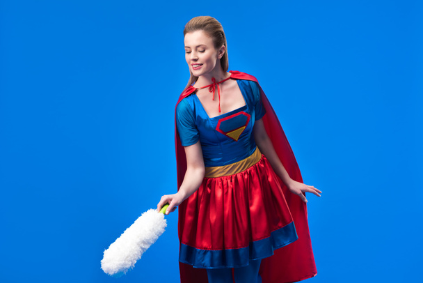 portrait of woman in superhero costume with dust cleaning brush isolated on blue - Photo, Image