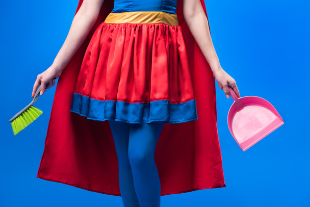 partial view of woman in superhero costume with broom and scoop for cleaning isolated on blue - Photo, Image