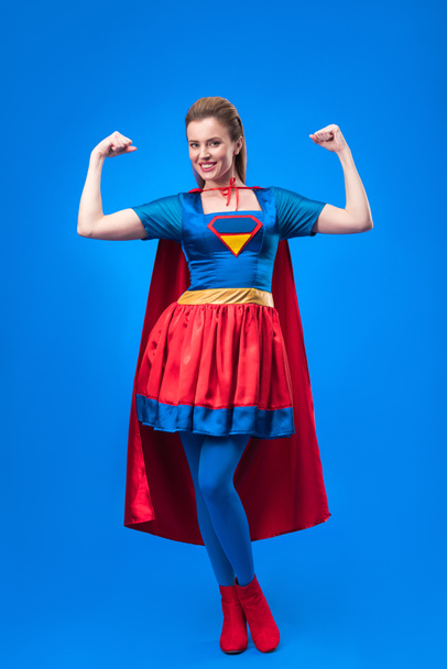 femme souriante en costume de super-héros montrant les muscles isolés sur bleu
 - Photo, image
