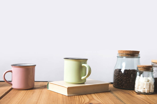 cups, book and glass bottles with coffee beans and refined sugar on table on white  - Foto, Imagem