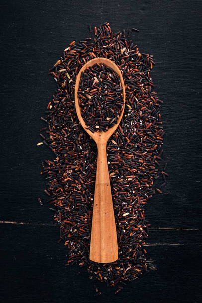 Black wild dry rice on a spoon. On a wooden background. Top view. Copy space. - Foto, Imagem