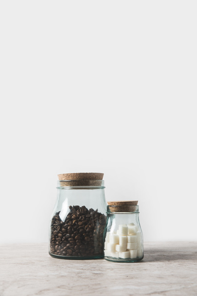 coffee beans and refined sugar in glass bottles on marble table on white  - Фото, изображение