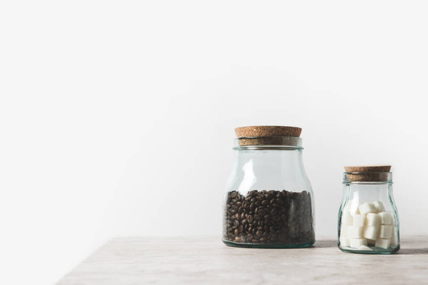 granos de café y azúcar refinada en botellas de vidrio sobre mesa de mármol sobre blanco
  - Foto, Imagen