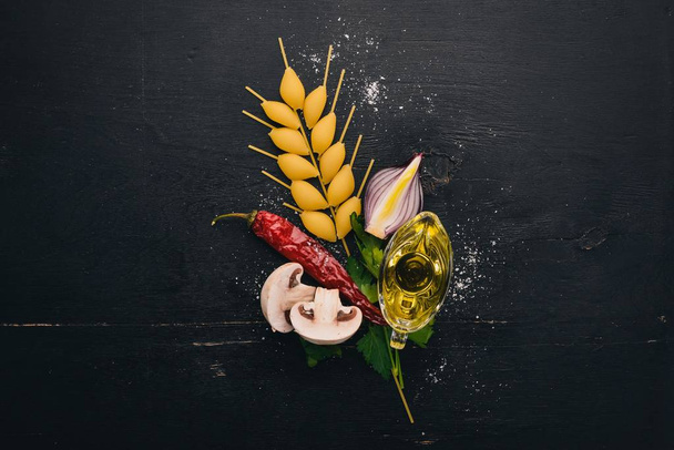 Dry pasta with fresh vegetables and spices. In the form of a spikelet of wheat on a wooden background. Top view. Copy space. - Фото, зображення