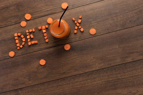 Inscription detox, carrot juice in a glass on a wooden background, top view. Concept of healthy eating, raw food diet, diet. - Zdjęcie, obraz