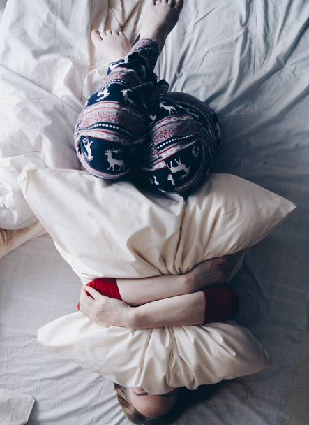 Happy girl in the winter clothes on white bed hugging a pillow. - Fotoğraf, Görsel