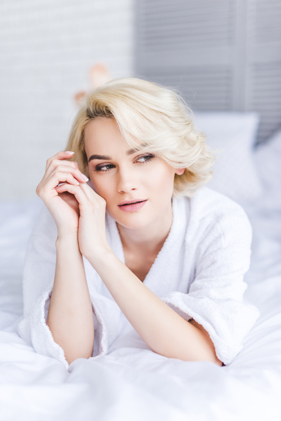 nachdenkliche attraktive blonde Frau im Bademantel schaut im Schlafzimmer weg - Foto, Bild