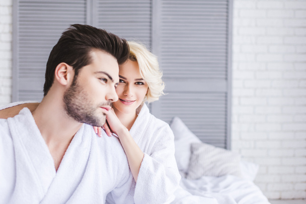 beautiful blonde woman smiling at camera while sitting with boyfriend on bed - Φωτογραφία, εικόνα