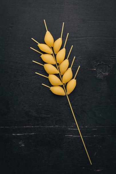 Dry pasta in the form of a spikelet of wheat on a wooden background. Top view. Copy space. - Foto, afbeelding
