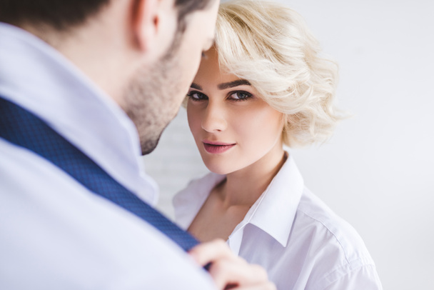young woman looking at camera while taking off necktie of boyfriend - Фото, изображение