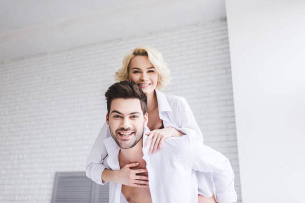 beautiful happy young couple piggybacking and smiling at camera at home  - Foto, immagini